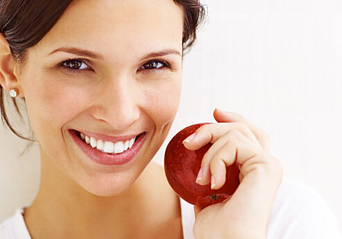 Portrait of happy young lady with a red apple smiling against white background